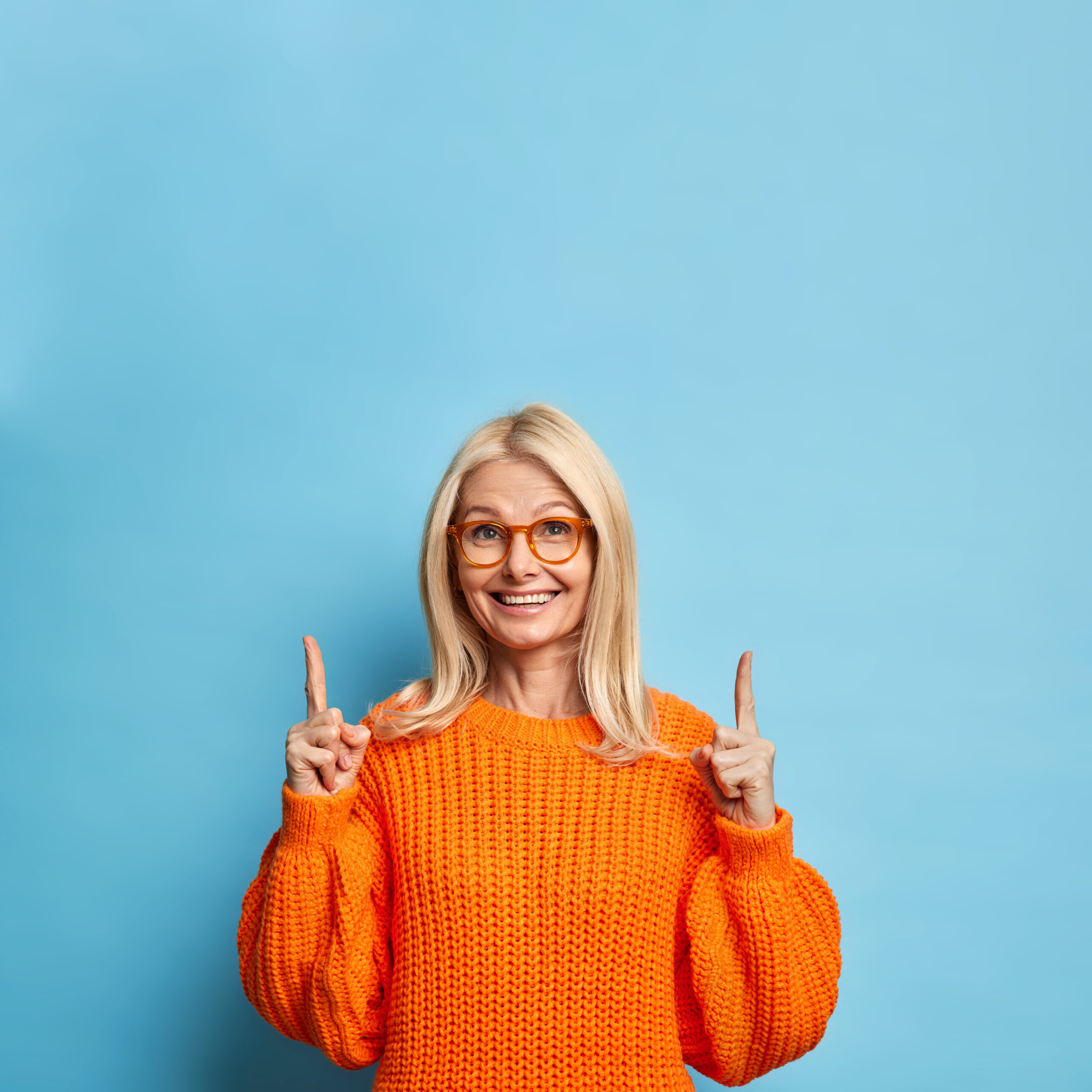 jolie blonde femme quarante ans sourit joyeusement pointant vers espace copie porte lunettes chandail orange scaled